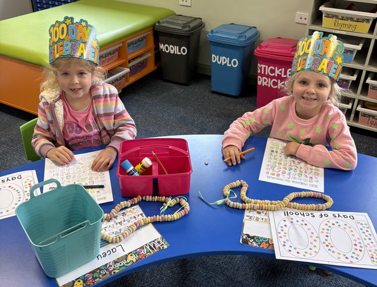 Two girls in Kindergarten sitting at a desk wearing party hats